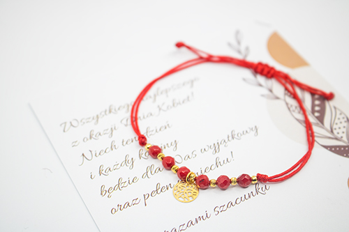 bransoletka z czerwonymi kamieniami i srebrnym, pozłoconym elementem w kształcie ażurowego kółeczka położona na karteczce z życzeniami - prezent na dzień kobiet